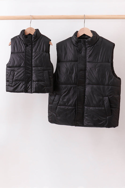 Two black puffer vests hanging on a rack against a white background
